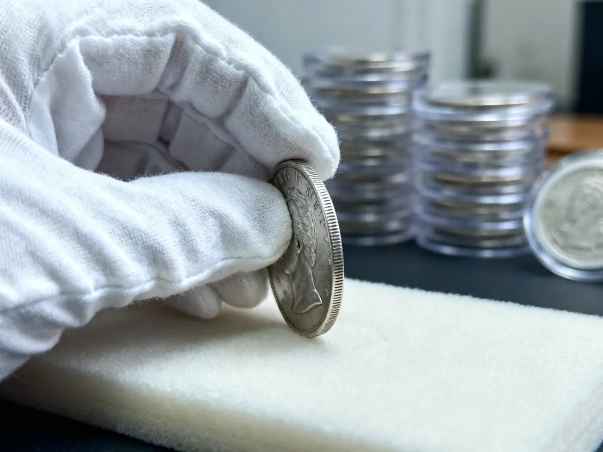 Kolekcjoner trzymający srebrną monetę za rant w rękawiczkach