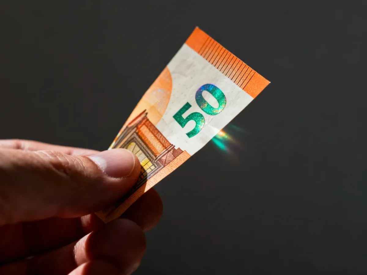 Przechylany banknot 50 euro z widocznym efektem hologramu i szmaragdowej liczby